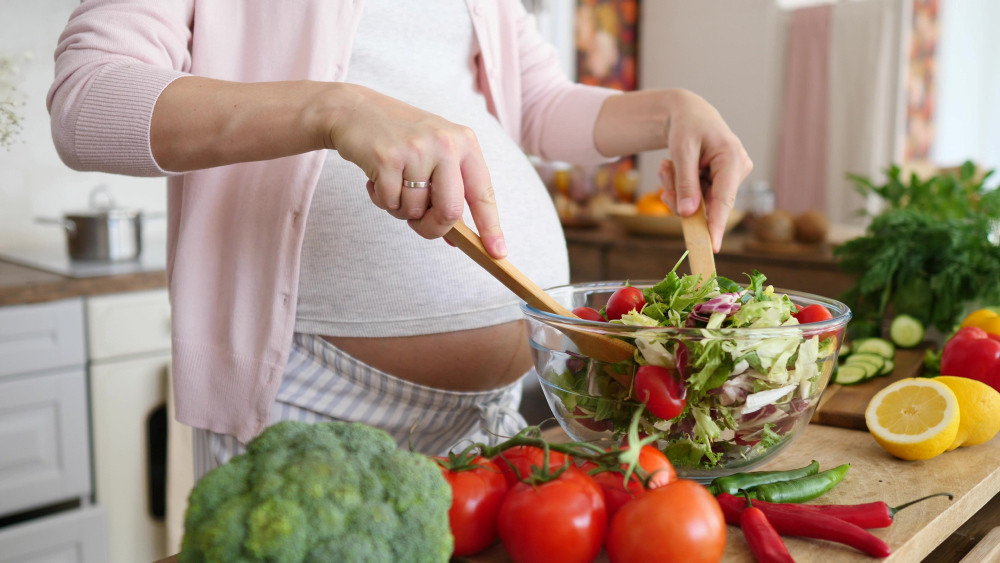 Schwangere bereitet Salat zu 
