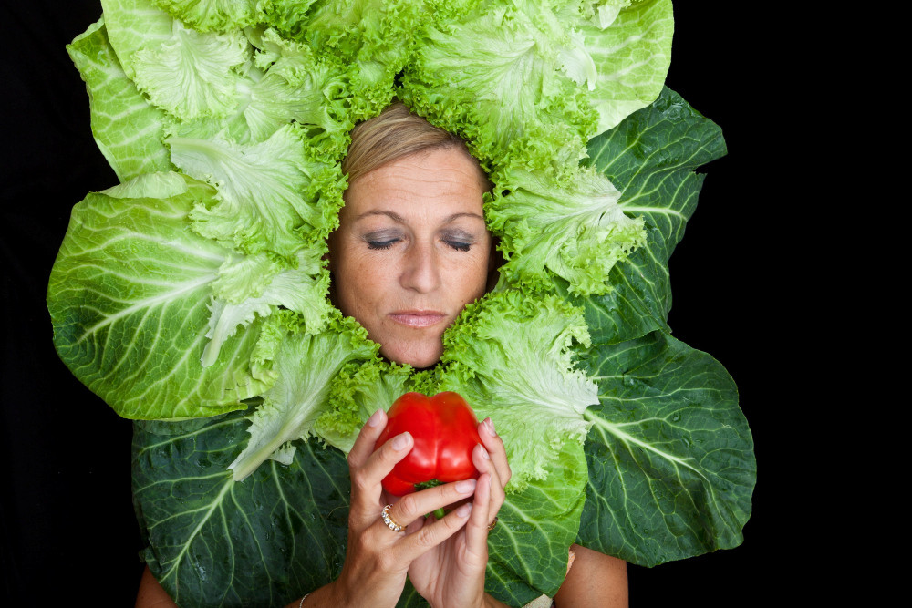 Frau mit Salatblattarrangement um den Kopf und einem roten Apfel in der Hand