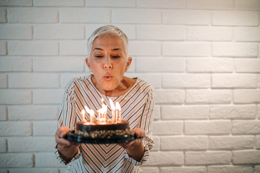 Ältere Frau pustet Kerzen auf einem Geburtstagskuchen aus