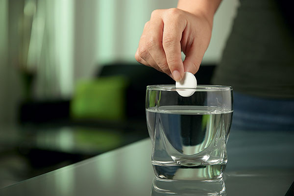 Weibliche Hand gibt Aspirin-Brausetablette in ein Glas Wasser