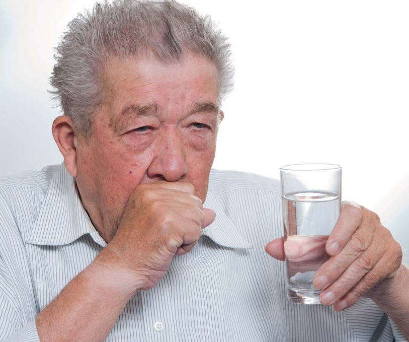 Älterer Mann hustet und hat ein Glas Wasser in der Hand