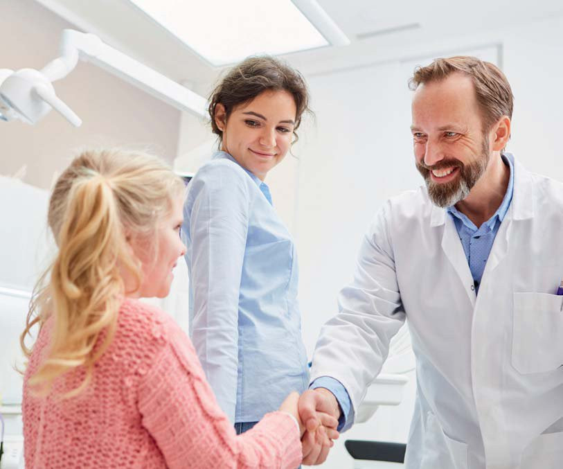 Arzt schüttelt Mädchen die Hand, Mutter lächelt
