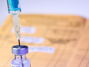 Spritze in Impfserum, Impfpass im Hintergrund