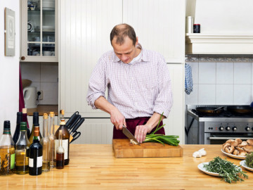 Mann in der Küche, schneidet Frühlingszwiebeln