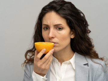 Frau riecht an Orange: Mit angenehmen Gerüchen, zum Beispiel dem einer Orange, können Menschen mit Migräne ihr Riechvermögen trainieren. Das kann sich auf den Verlauf der Migräne auswirken.