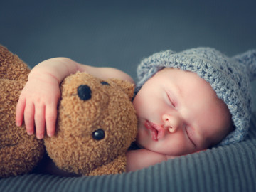 Neugeborenes schläft mit Teddy im Arm