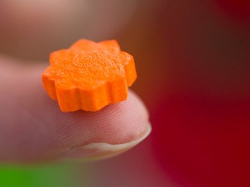 Orangefarbene Ecstasy Tablette in Großaufnahme auf einem Zeigefinger gehalten