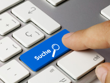 Finger auf blauer Tastaturtaste mit der Beschriftung „Suche“ und Abbildung einer Lupe