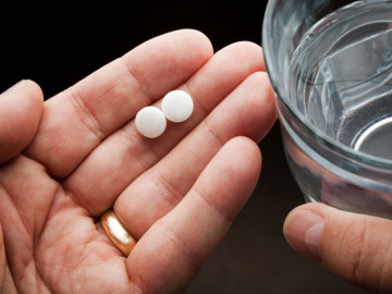 Linke Hand hält zwei Tabletten, rechte ein Wasserglas