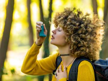 Frau im Wald mit Wanderrucksack nutzt Asthmaspray