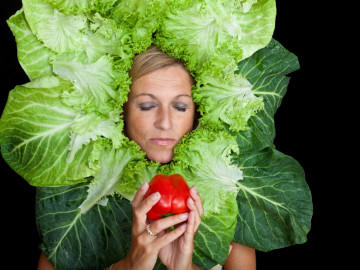 Frau mit Salatblattarrangement um den Kopf und einem roten Apfel in der Hand
