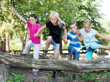 Vier Kinder springen über einen Baumstamm