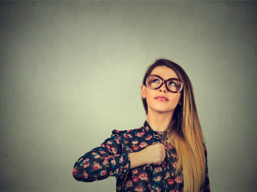 Superhero girl. Confident young woman in glasses isolated on gray wall background. 